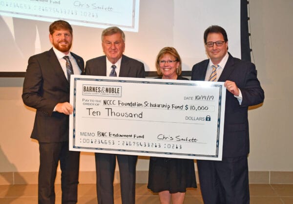 Four people in formal attire smile while holding a large ceremonial check for $10,000 made out to the NCCC Foundation Scholarship Fund from Barnes & Noble, dated 10/19/19.