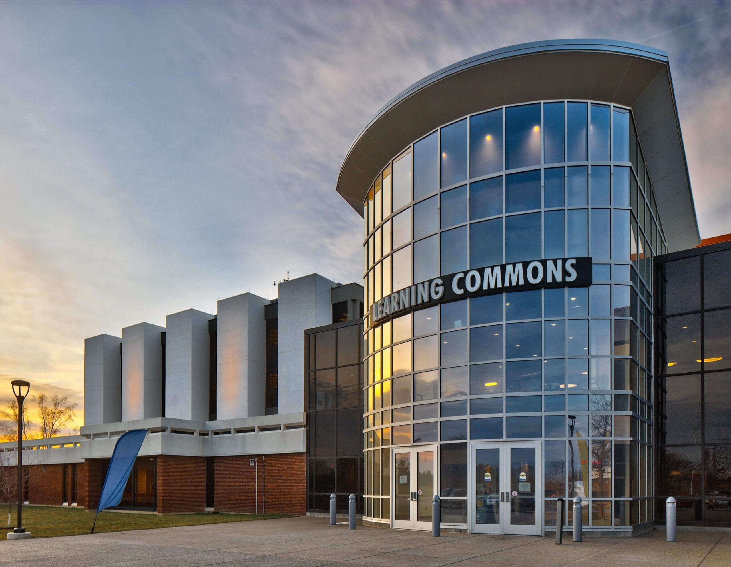 Photo of the Learning Commons. Tall glass building in front of a sunset.