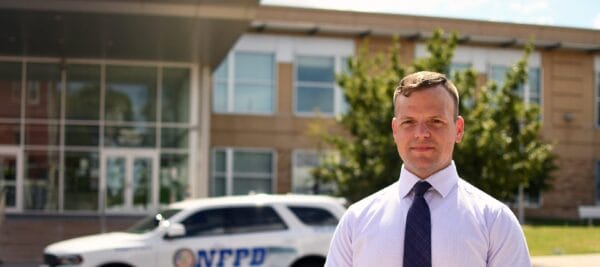 Photo of a police officer standing in front of a police car.