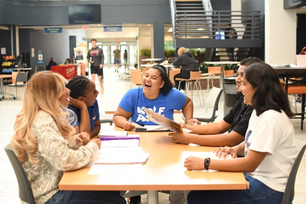 Five students sitting at a table laughing and studying.