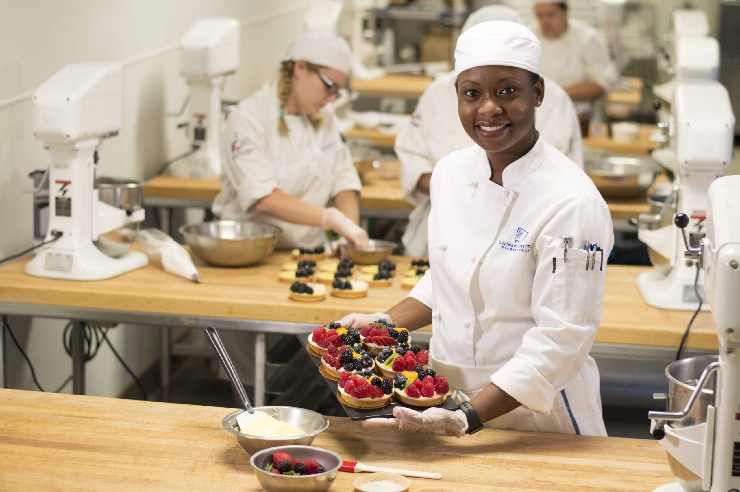 Baking student holding a trey of pastry's with fruit on them in a baking class.