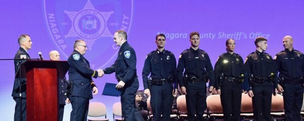 Police officers standing in a line while two are shaking hands on stage at a ceremony.