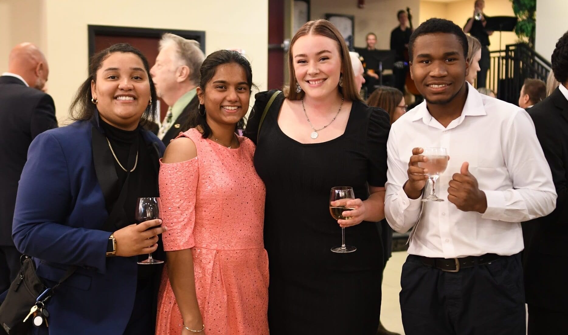 Four students smiling drinking out of wine glasses at a formal party.