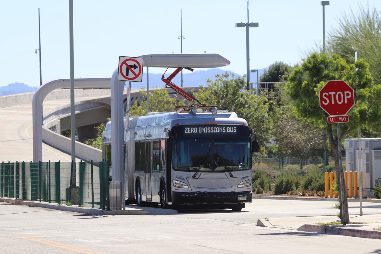 Electric Bus Charging with Pantograph next to a highway and foliage