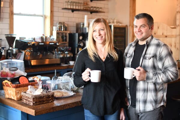 A woman and a man stand side by side in a cozy coffee shop, each holding a white mug and smiling—showcasing the support of the Small Business Development Center at SUNY Niagara: Your Partner in Business Success.