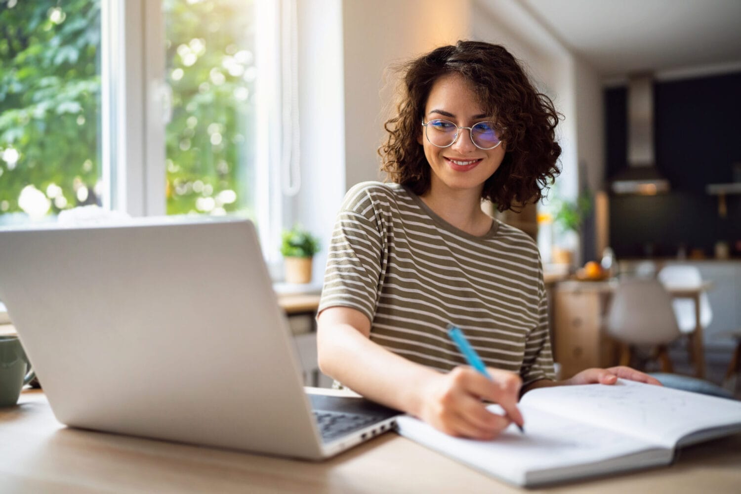 Girl working on laptop and writing notes at home