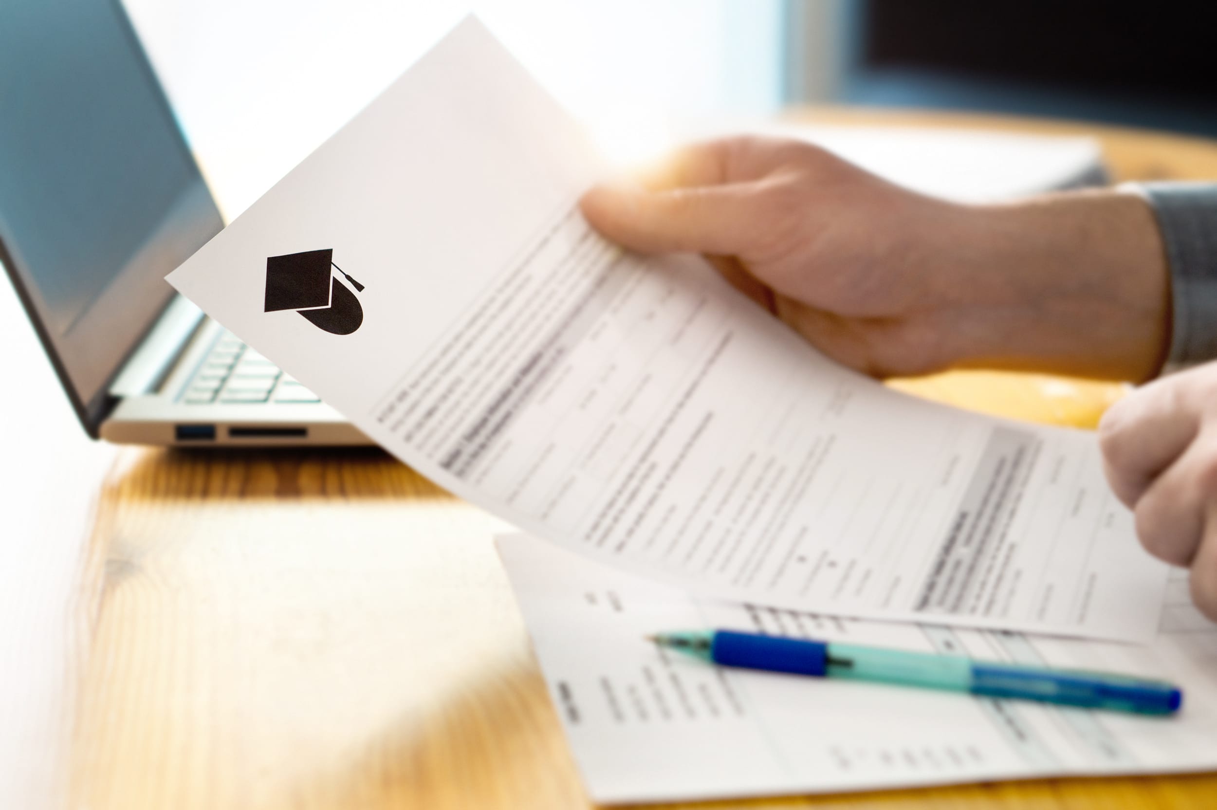 Close-up of hand filling out form next to laptop