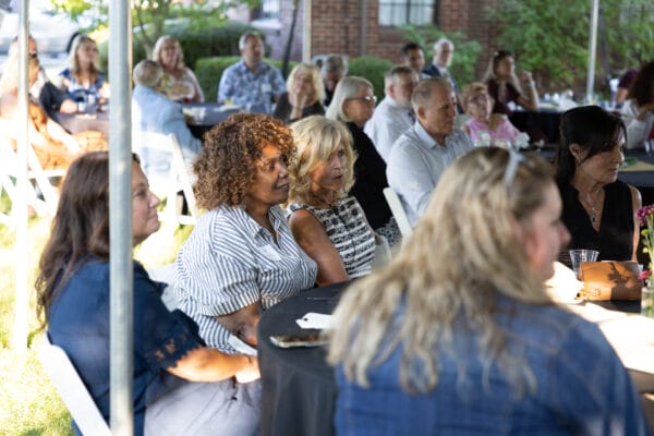 People sitting at round tables watching a speaker under a white tent at the 2025 Presidents Circle reception