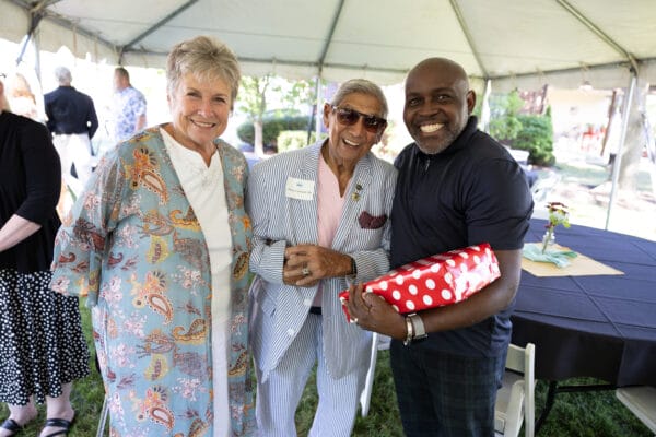 Two people under a white tent with SUNY Niagara's president Dr. Holmes smiling holding a wrapped red present at the 2025 Presidents Circle reception