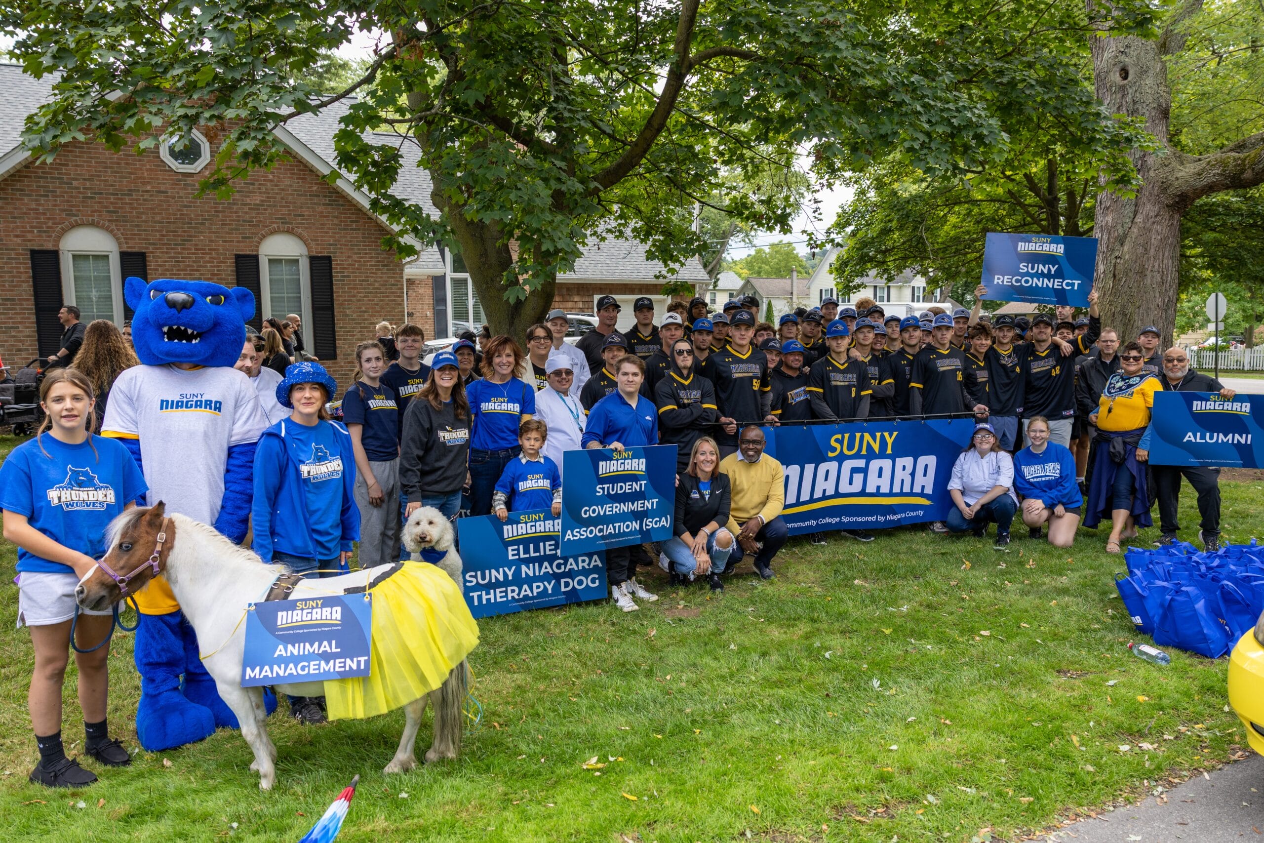 A large group of SUNY Niagara students, staff, and mascots gather outdoors holding signs for campus organizations, showcasing Campus Life at SUNY Niagara: Engaging Events and Leadership Opportunities for Student Development.