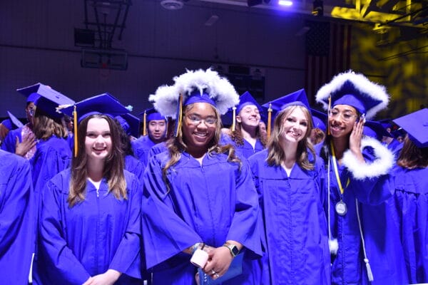 A group of graduates in blue caps and gowns smile and pose together indoors at a graduation ceremony. Some wear honor cords and fluffy white-trimmed stoles, celebrating their achievements with Welcome to ACE: Empowering Your Academic Success at SUNY Niagara.