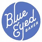 Blue circle logo with the words Blue Eyed Baker written in a playful white cursive font, with Baker in smaller uppercase letters aligned vertically on the right.
