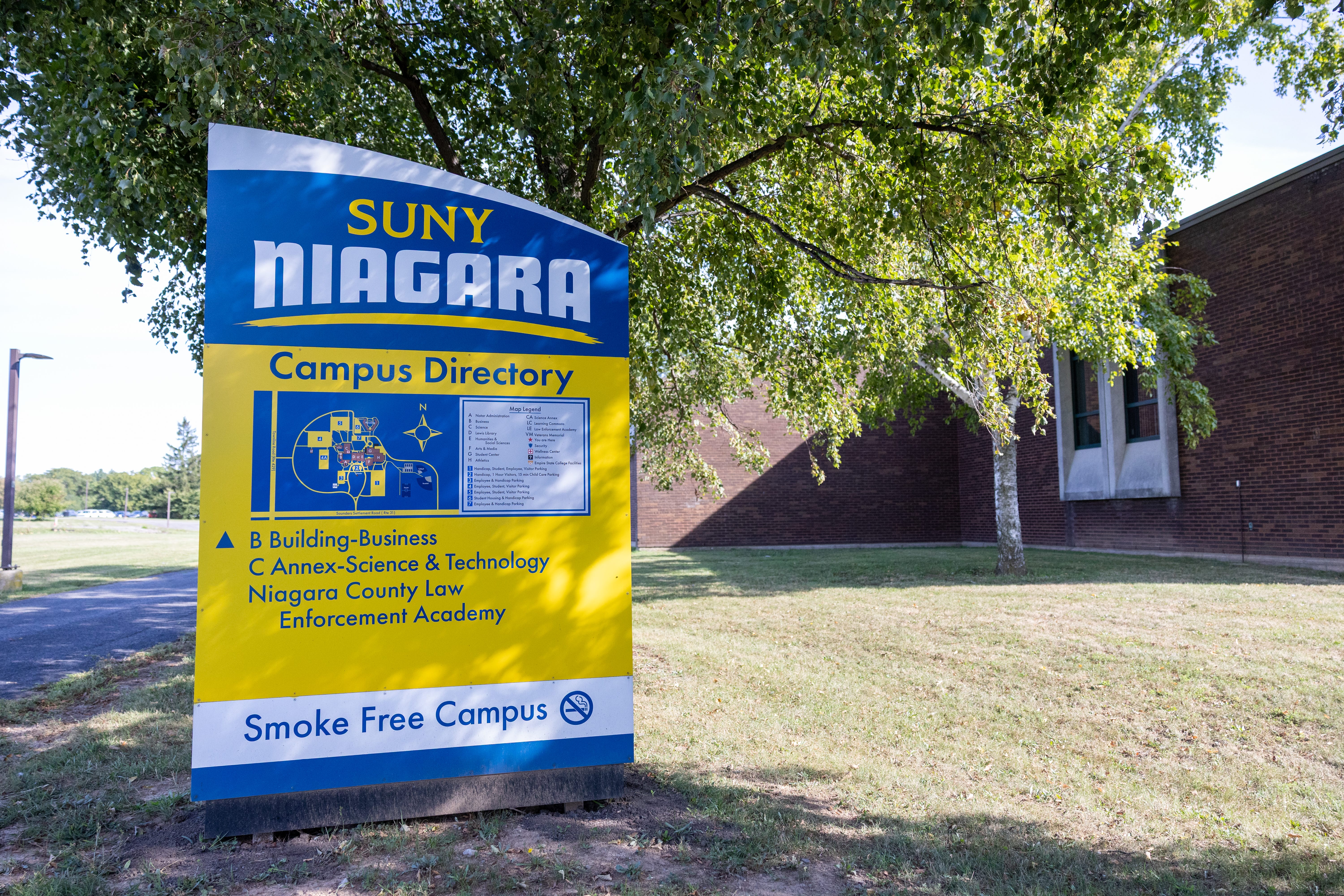 A large sign in front of a building displays SUNY Niagara with a campus directory map, building listings, and a Smoke Free Campus notice. Trees and a brick building are visible in the background.