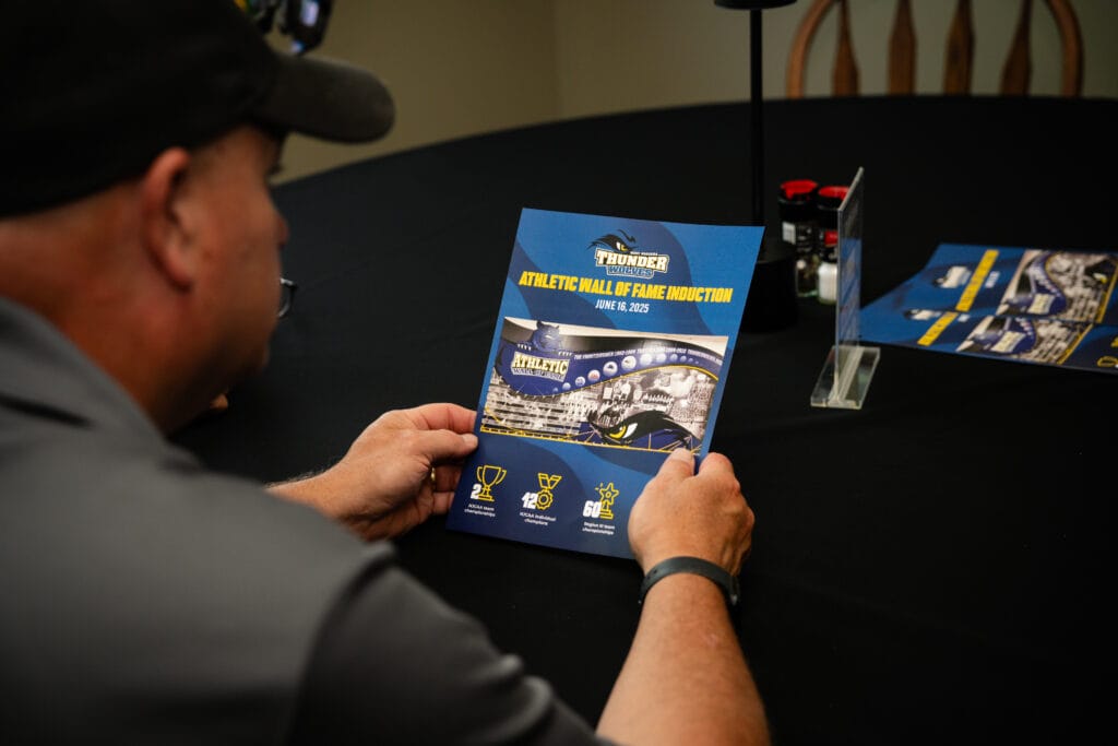 A man holding a blue and yellow brochure from the Forever Connected: SUNY Niagara Alumni Association.