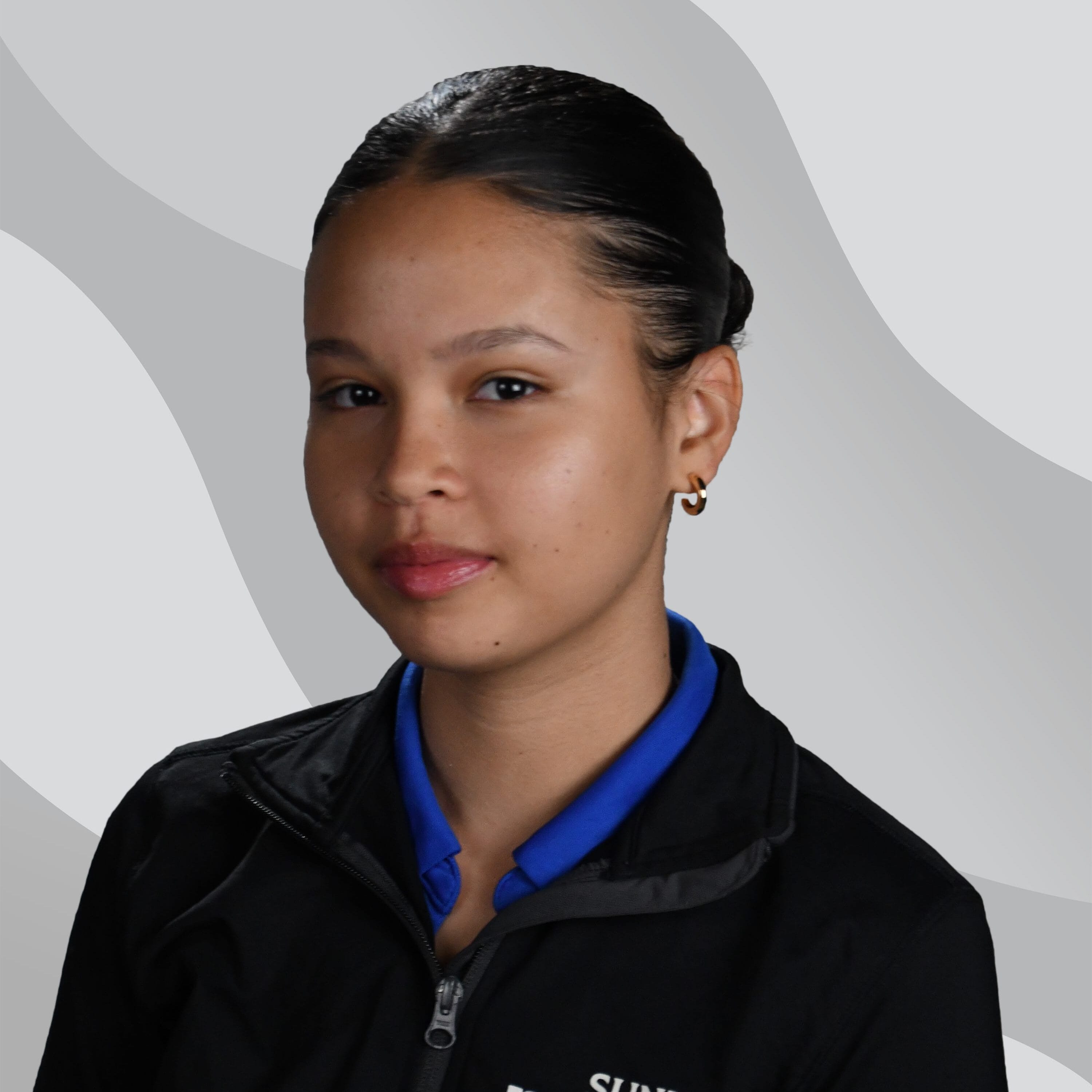 A young woman with dark hair pulled back, wearing a blue collared shirt and a black jacket with SUNY Niagara Child Development Center embroidered on it, sits in front of a light gray patterned background.