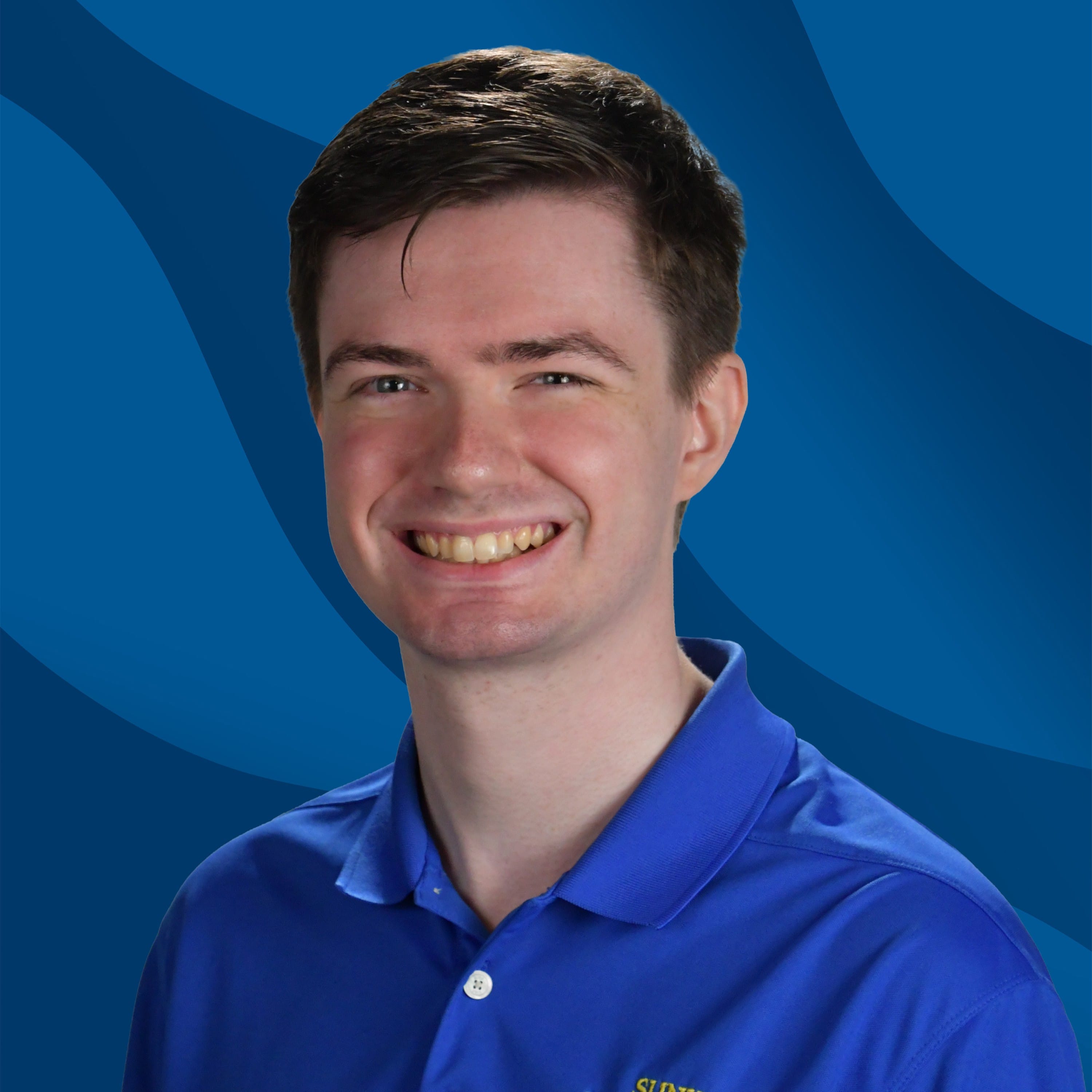 A young man with short brown hair smiles, wearing a blue collared shirt, posed in front of a blue abstract wavy background.