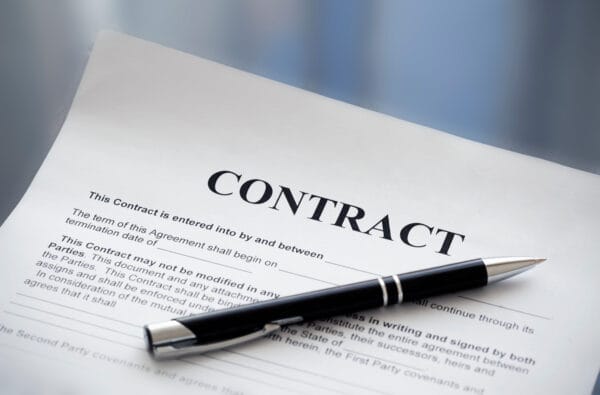 A black pen rests on top of a printed contract document with blank spaces for names and dates, ready to be filled in and signed.