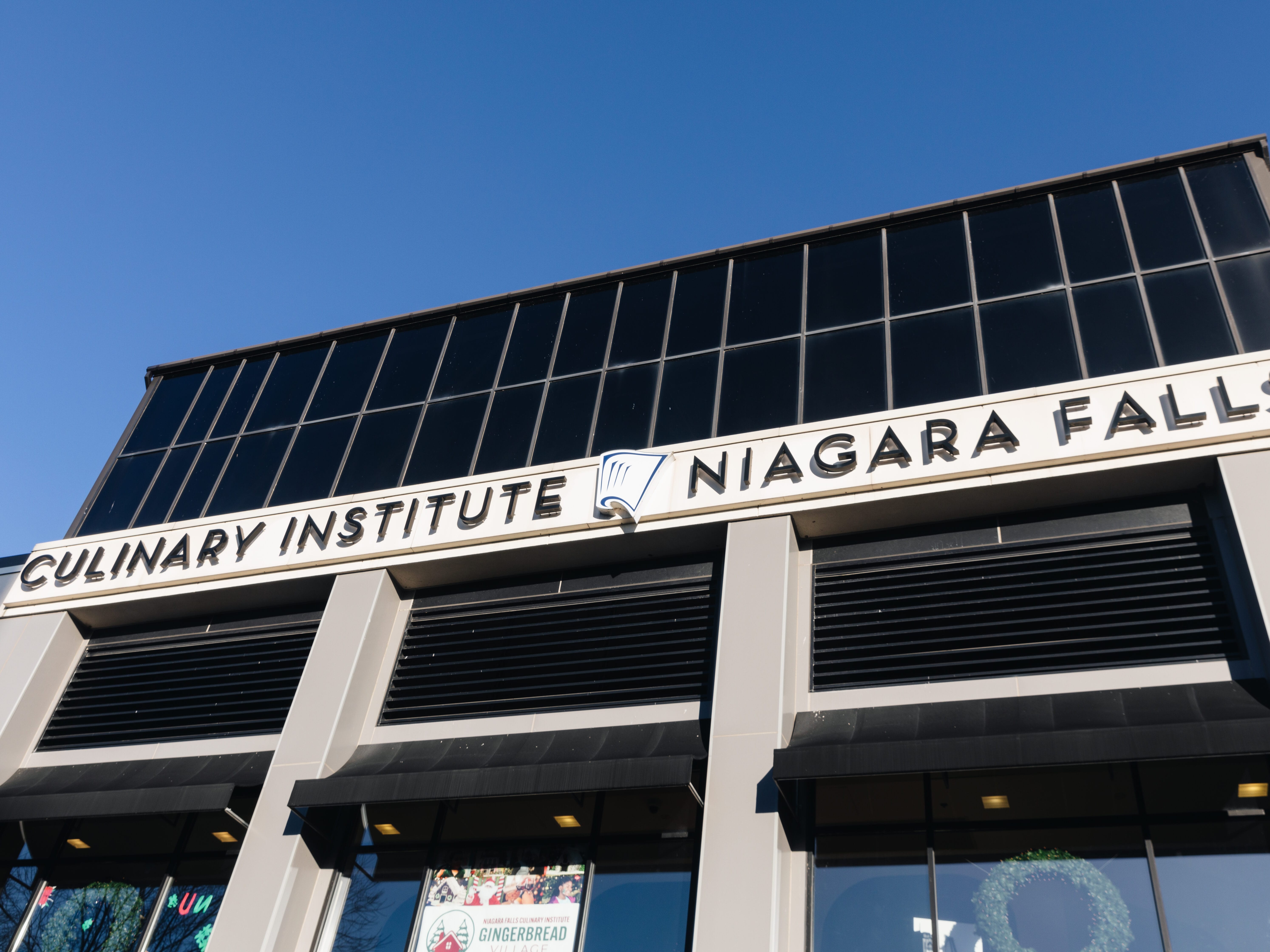 The exterior of the Culinary Institute Niagara Falls building with a clear blue sky above and the institutes sign prominently displayed.
