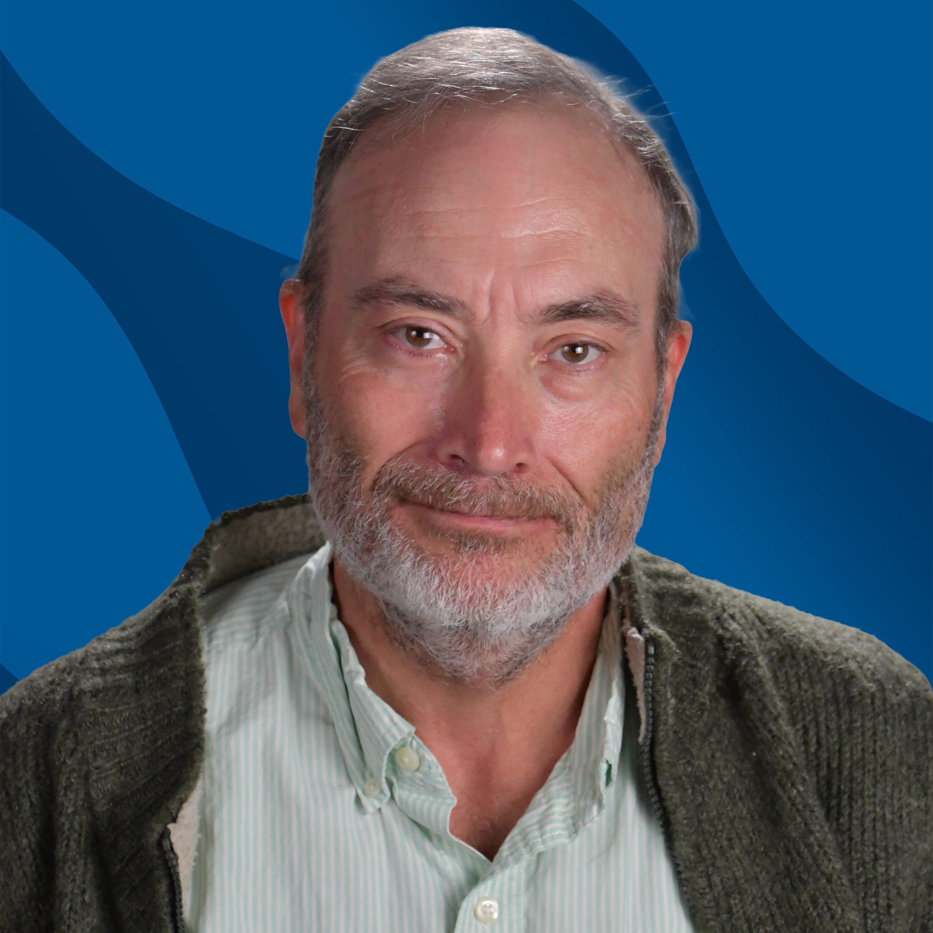 A middle-aged man with gray hair and beard smiles softly, wearing a green sweater over a light green striped shirt. He has a pen in his shirt pocket, and the background is blue with wavy patterns.