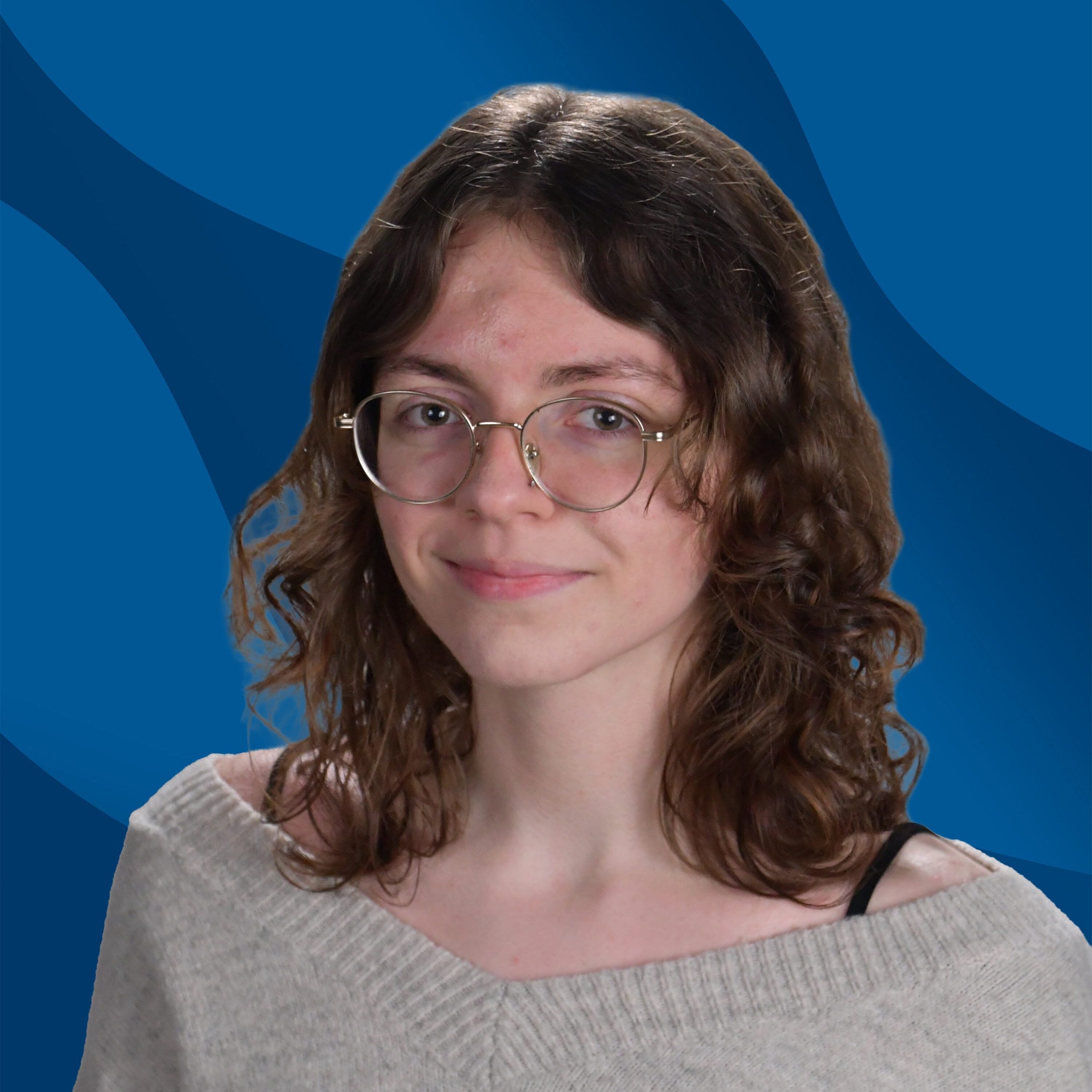 A young person with wavy brown hair, glasses, and a light sweater smiles slightly in front of a blue, wavy-patterned background.