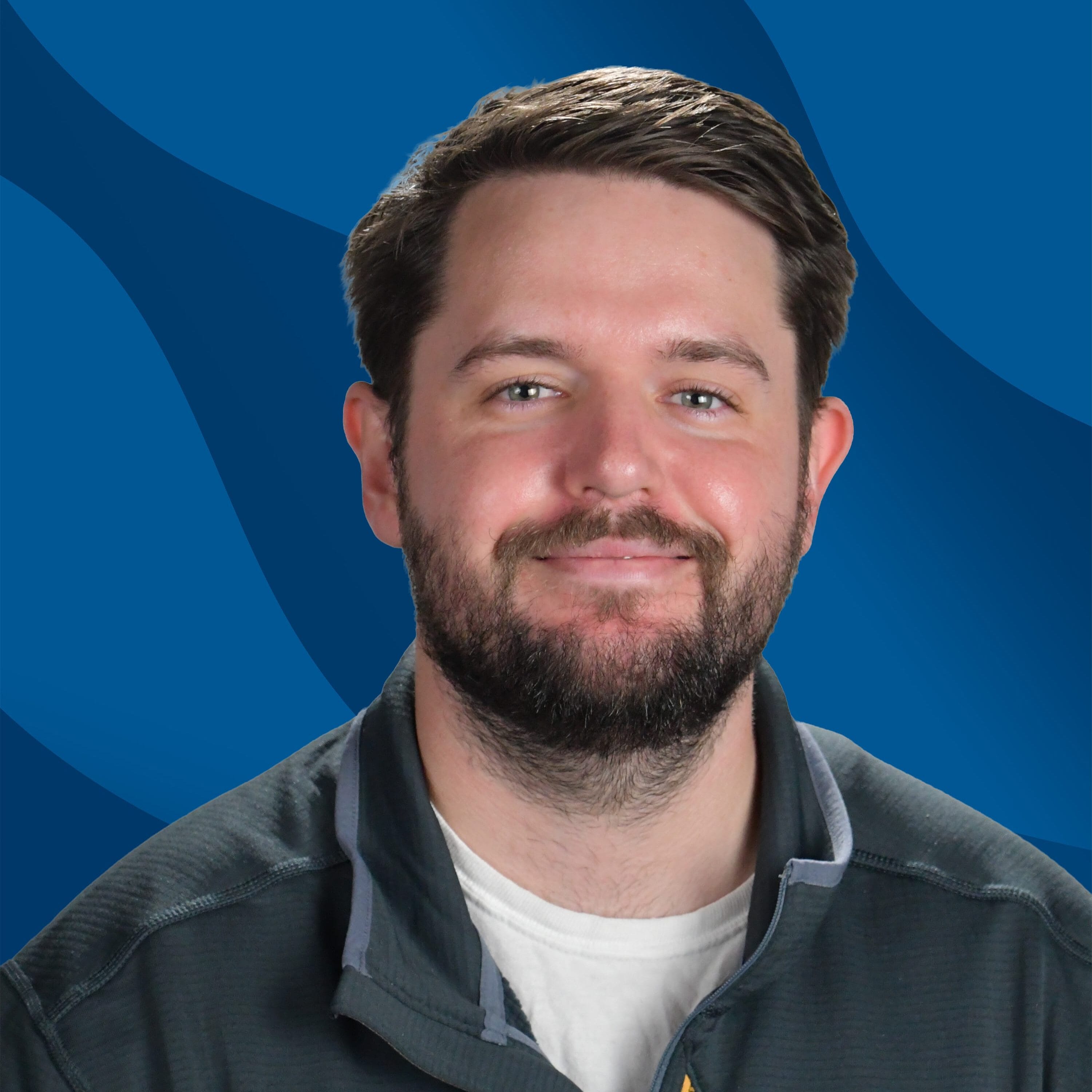 A portrait of a smiling man with a beard, wearing a dark zip-up jacket over a white shirt. He wears a SUNY Niagara name tag that reads Stephen S., Academic Center for Excellence. The background is a blue graphic design.