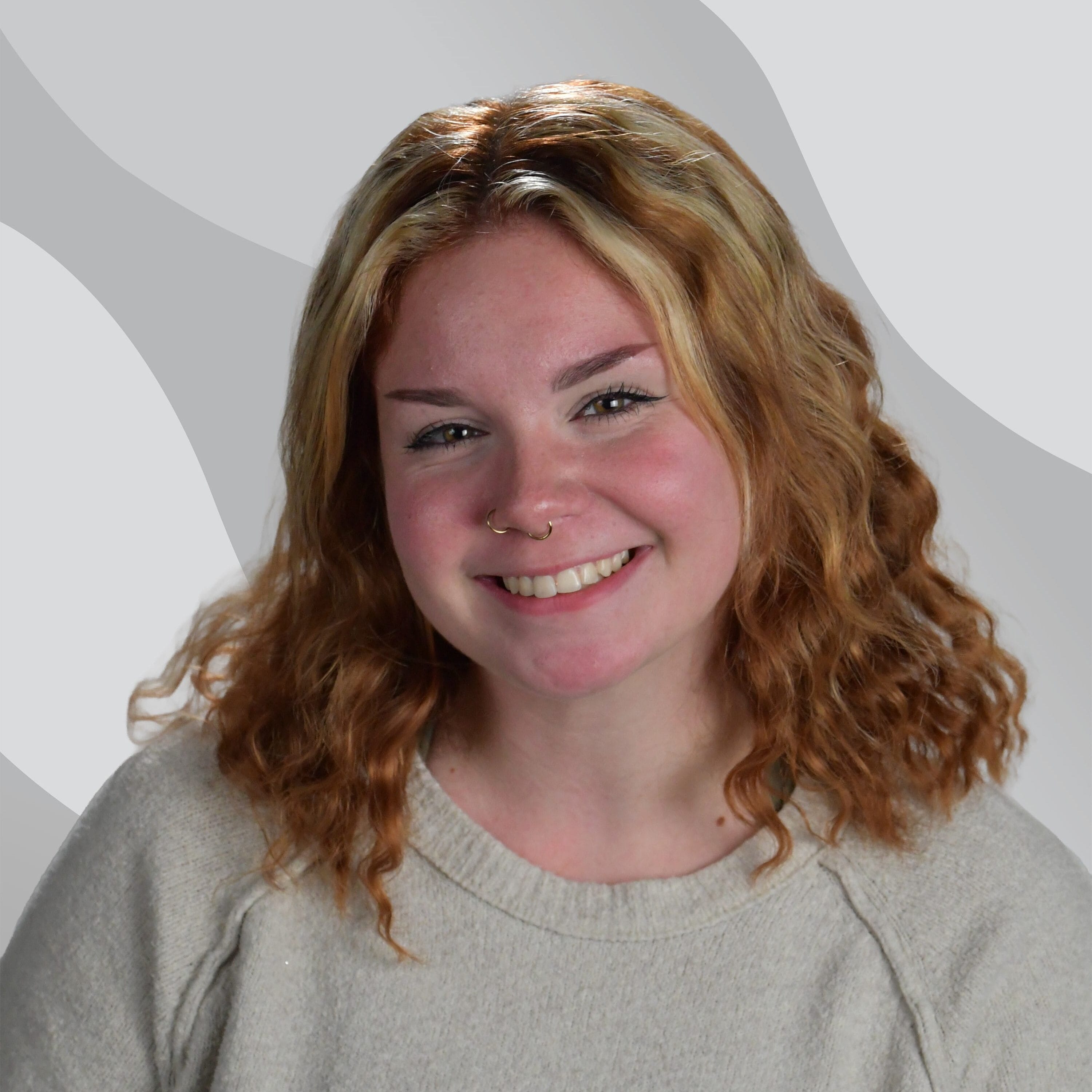 A smiling young woman with wavy hair and a nose ring.