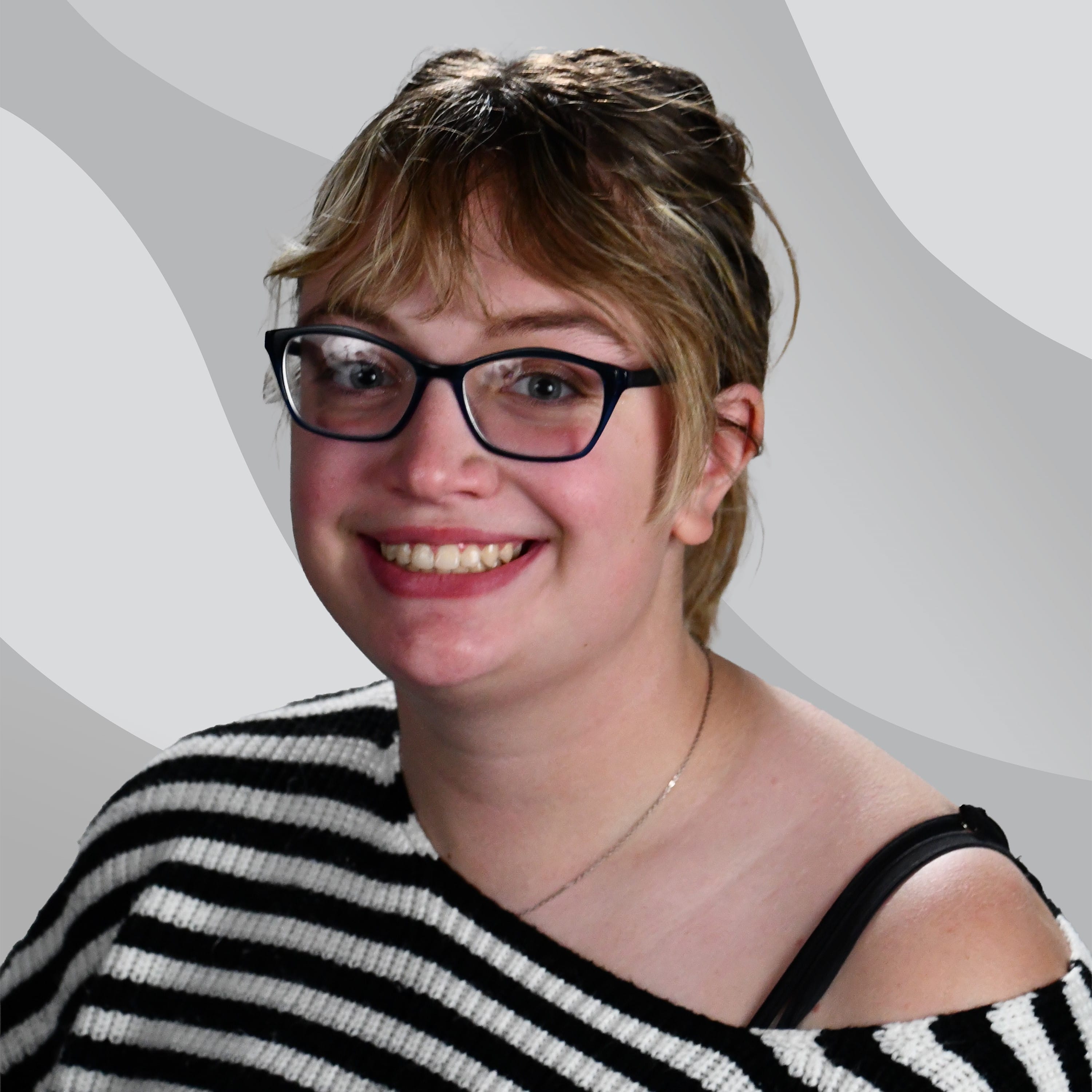 A smiling young person with blonde hair and glasses wearing a black and white striped sweater.