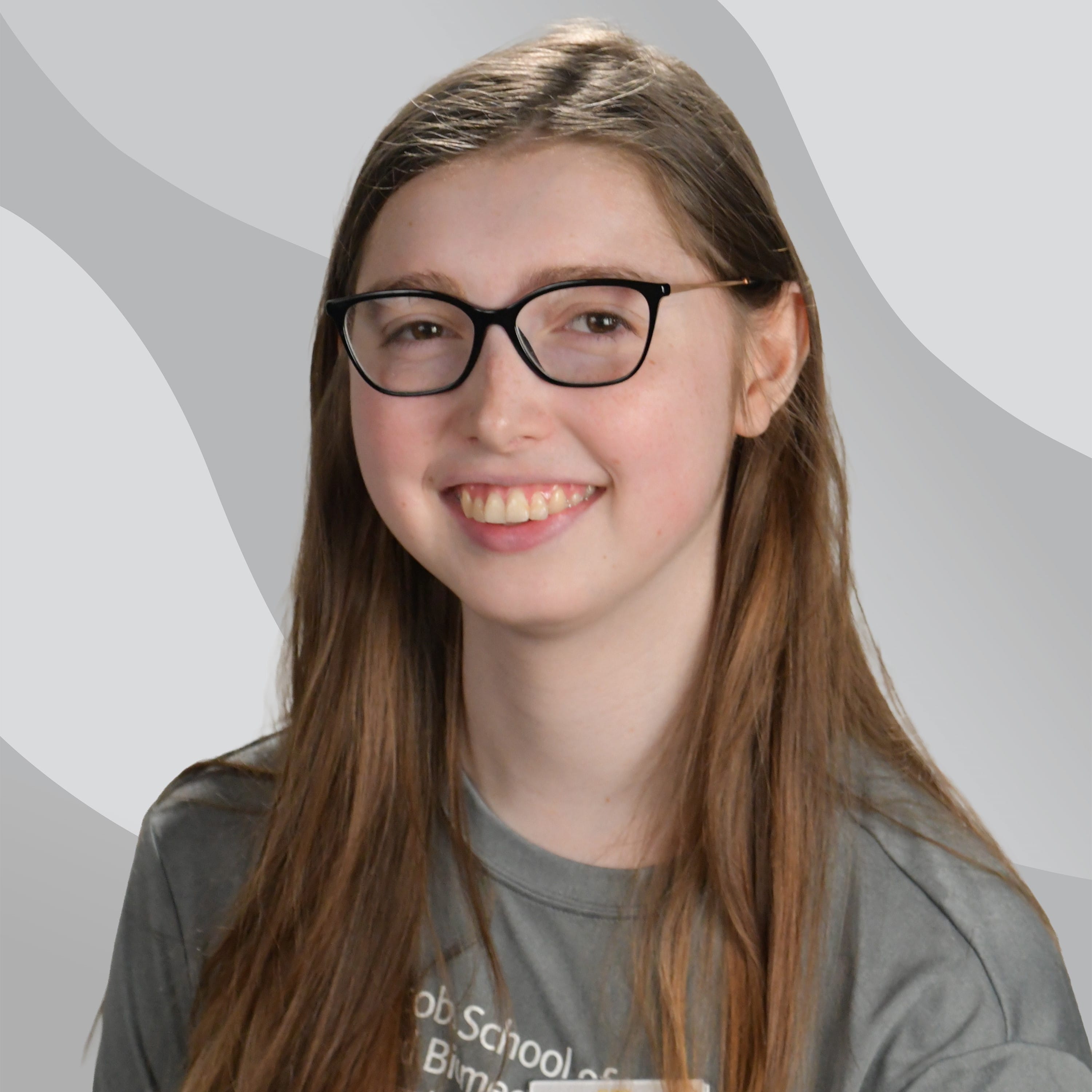 A young woman with long brown hair wearing black-rimmed glasses and a grey t-shirt smiles at the camera.