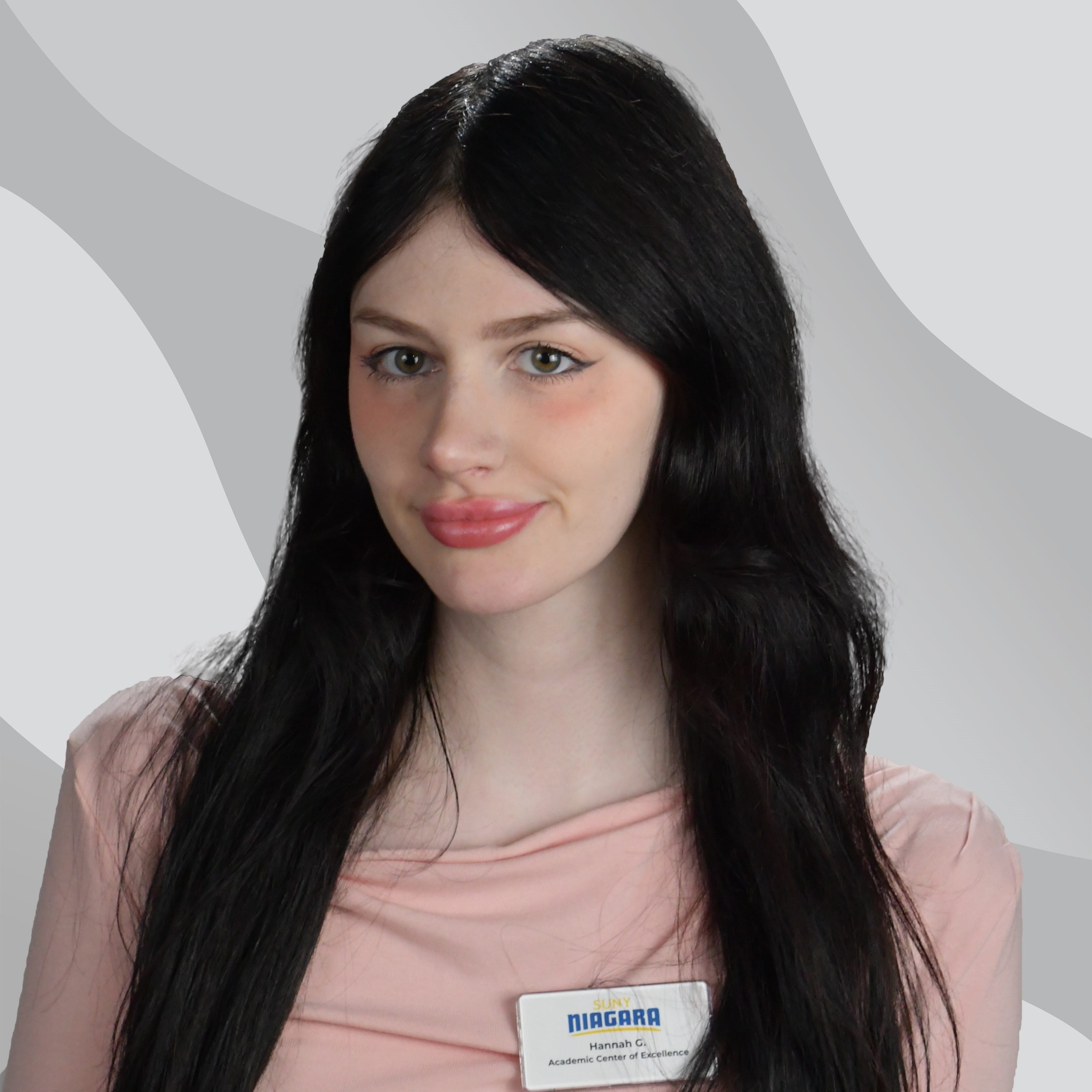 A young woman with long dark hair wearing a light pink top and a SUNY Niagara Academic Center of Excellence name tag.