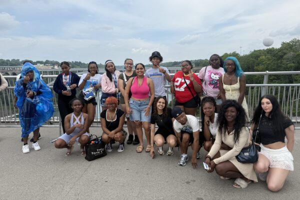A group of young people posing for a photo on an observation deck overlooking a river.