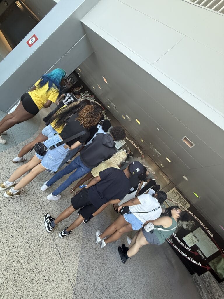 A group of young people stand in a line indoors, looking at informational wall displays.