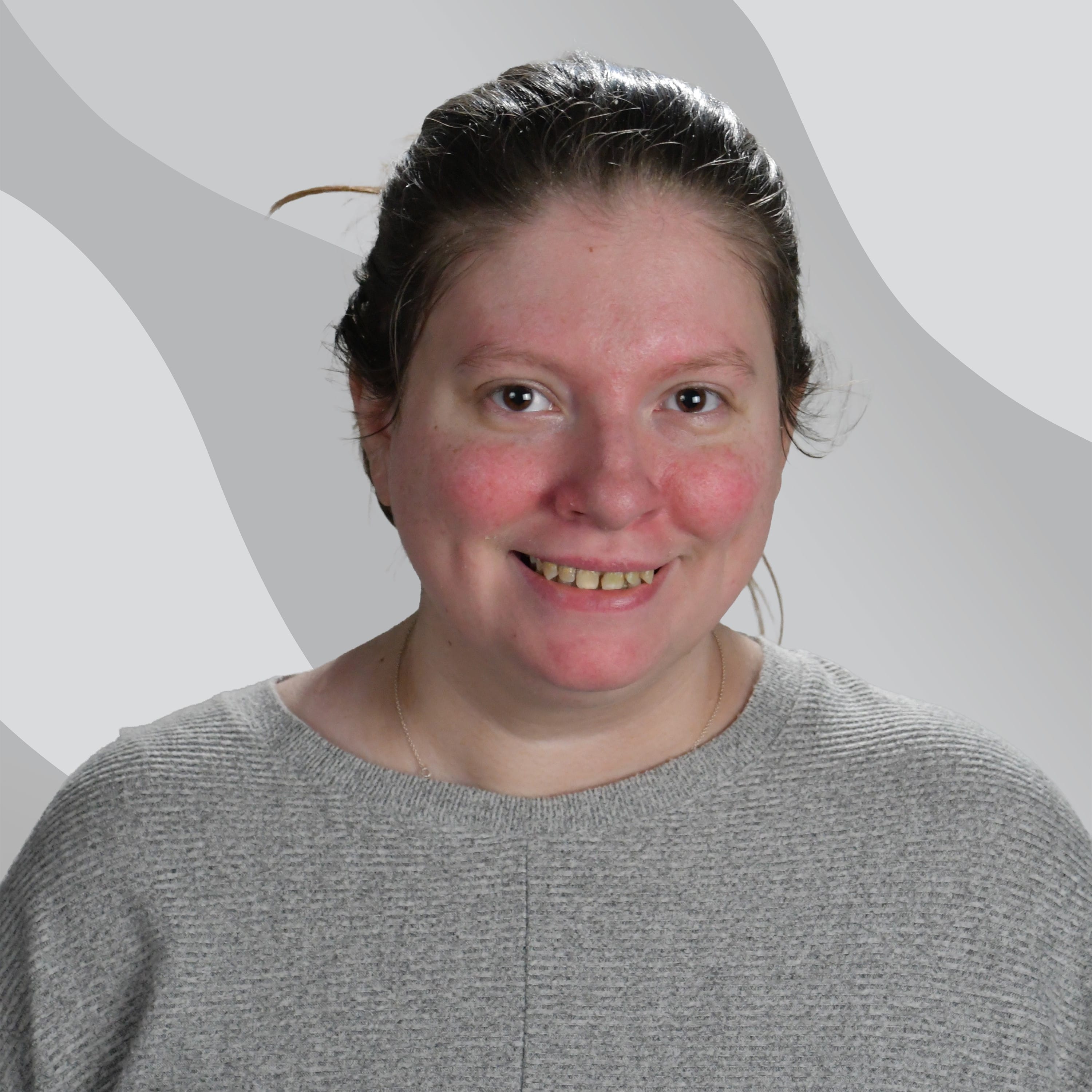 A smiling woman with her hair pulled back, wearing a grey sweater.