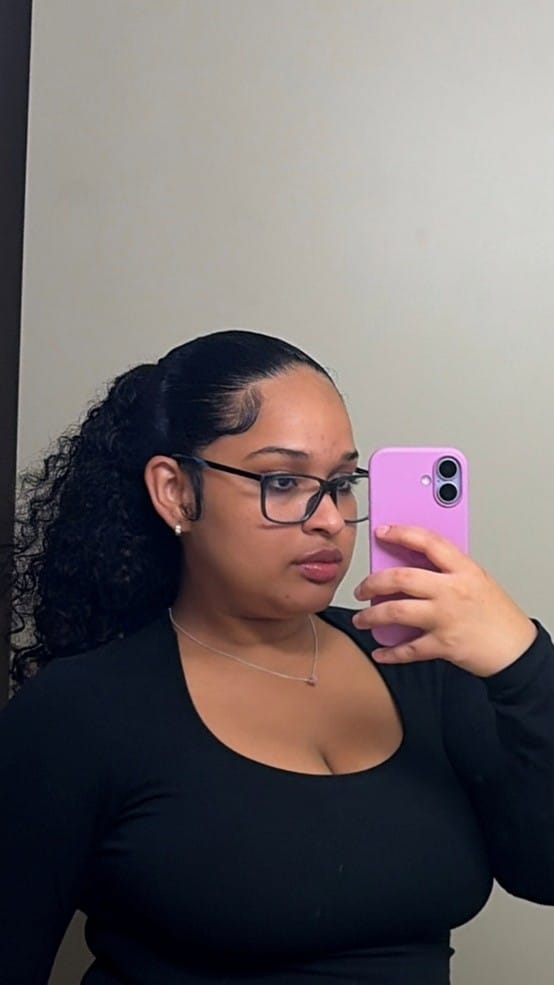 A woman with a high ponytail and glasses takes a mirror selfie with her purple smartphone, supporting the Educational Opportunity Program at SUNY Niagara.