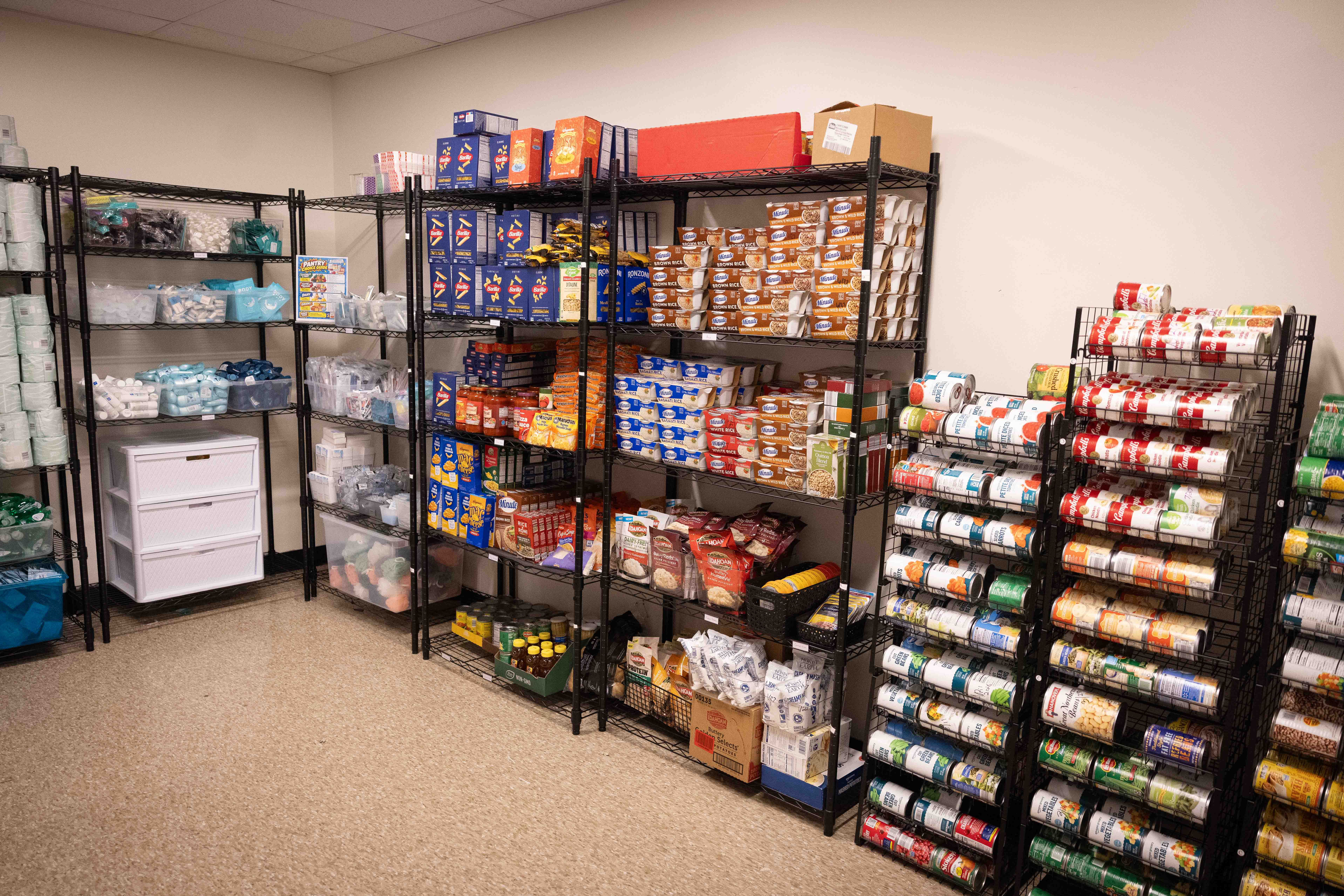 Metal shelving units in a pantry filled with food items including canned goods, boxes of pasta and rice, and small packages of snacks.