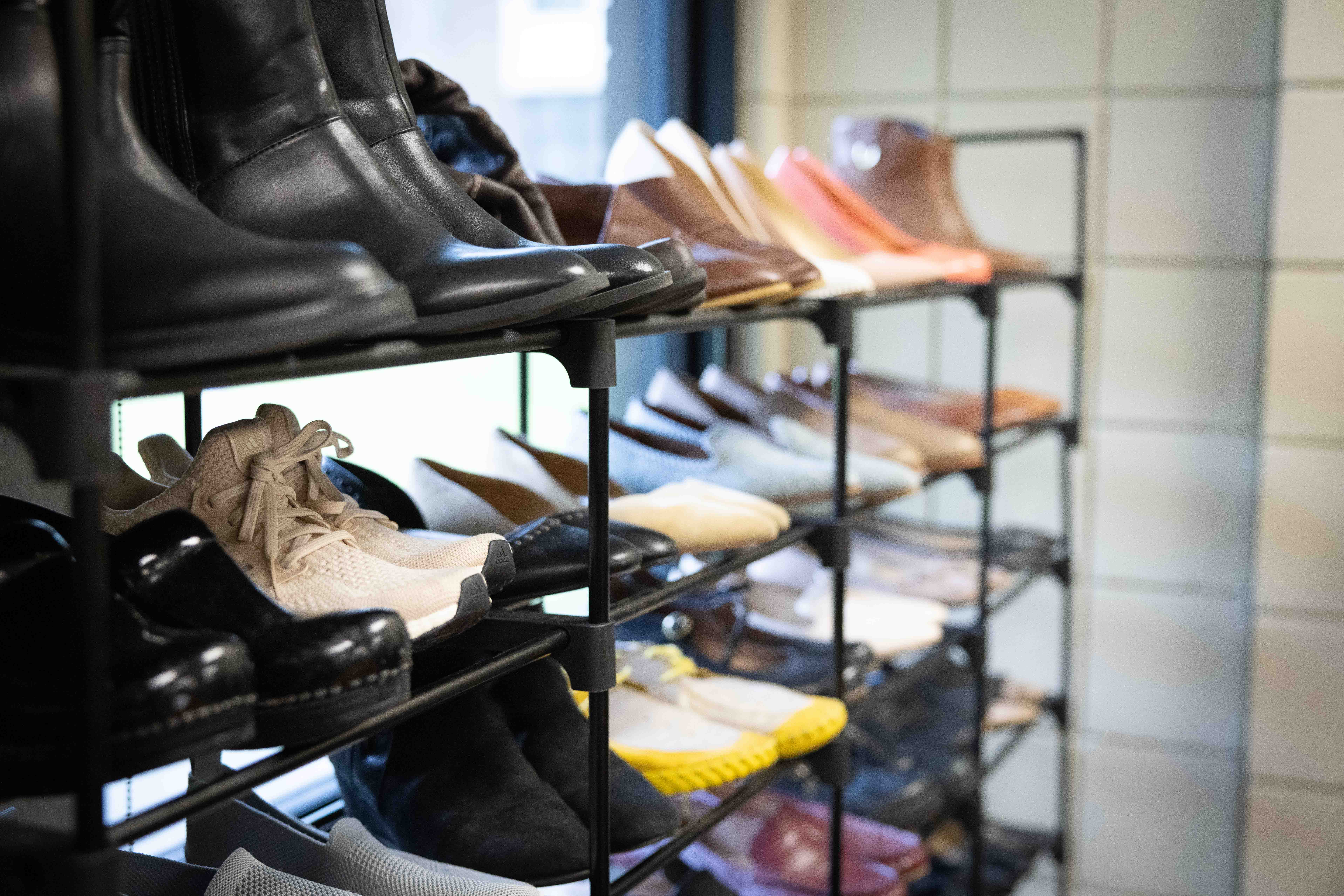 A metal shoe rack filled with various styles of footwear, including boots, sneakers, loafers, and clogs.